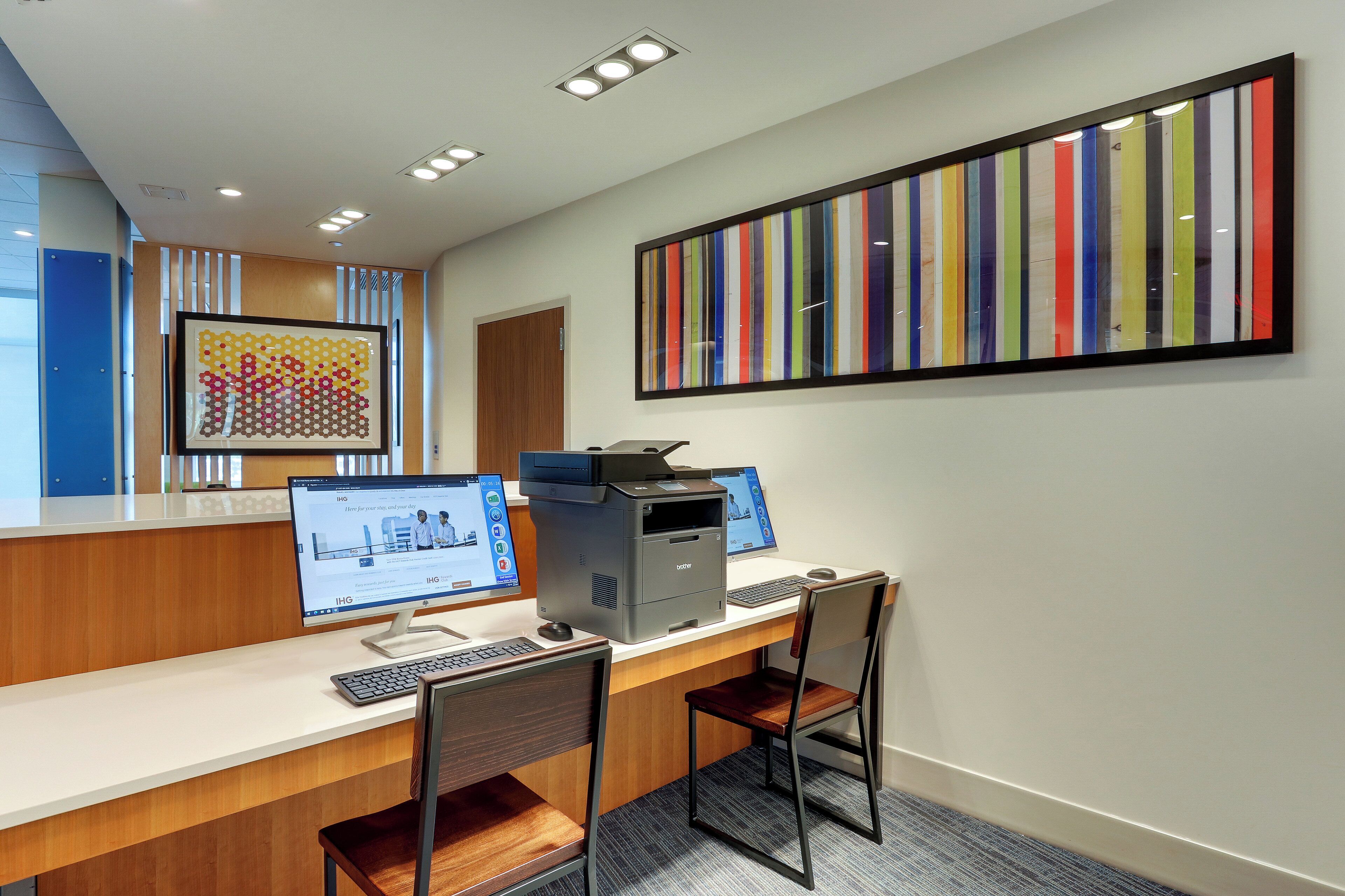 A modern office space with desks, computers, and a large colorful artwork on the wall.