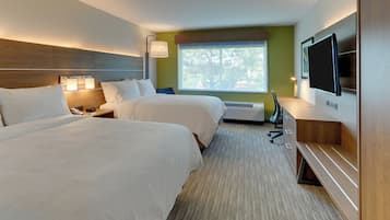 Habitación de hotel con dos camas, televisión, escritorio y ventana con vista a árboles.