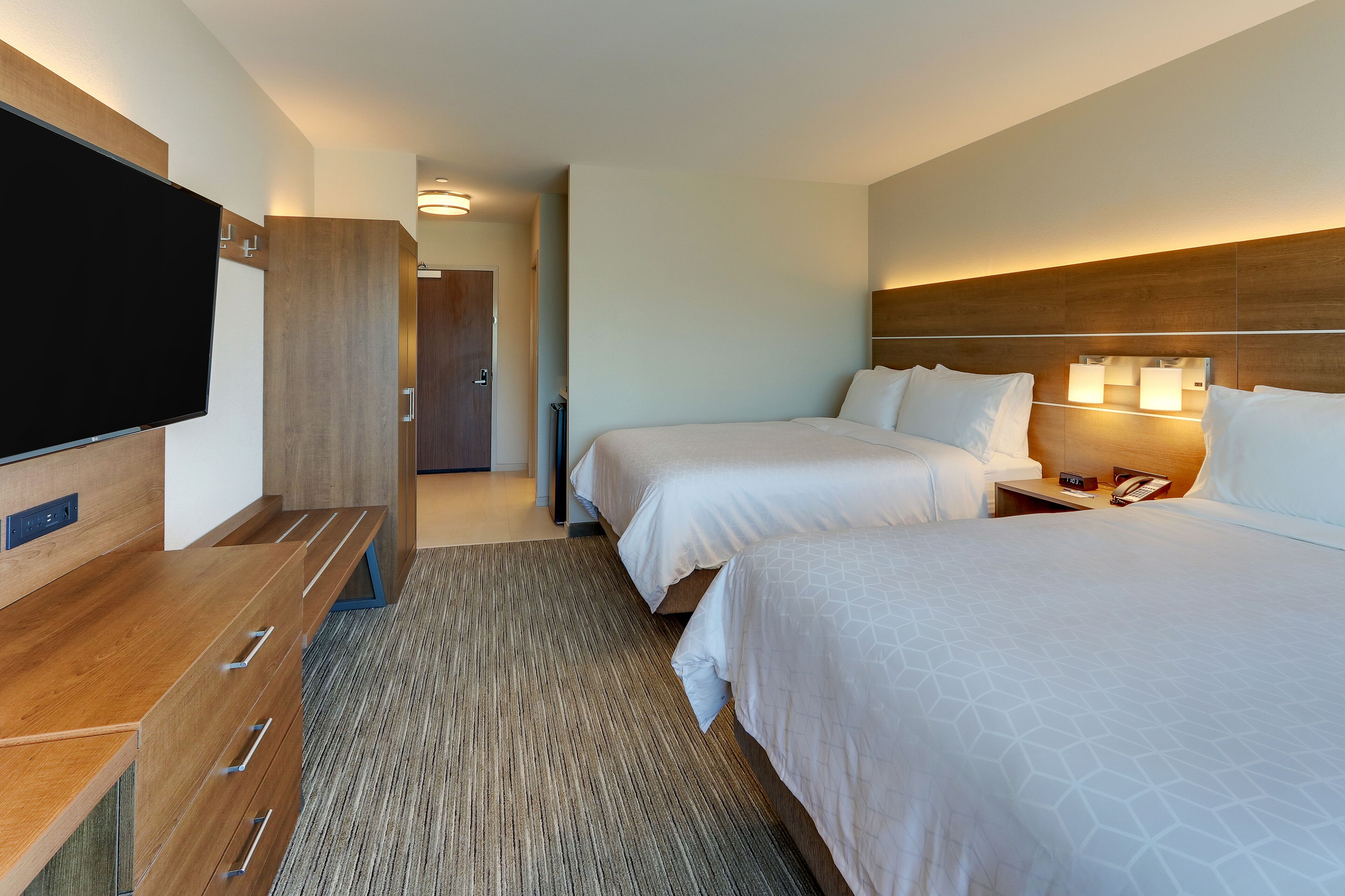 A hotel room with two beds, a TV, a wooden desk, and a carpeted floor.