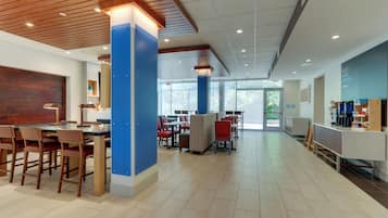 A modern cafe with wooden ceiling, blue pillars, and a variety of seating options including tables and chairs.