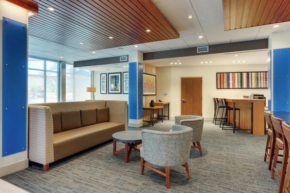 A modern lobby with a sofa, chairs, a small table, and a reception desk. - Holiday Inn Express & Suites Roanoke – Civic Center by IHG (Roanoke)