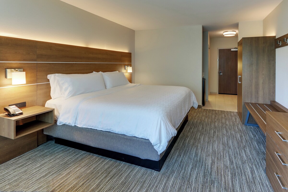 A modern hotel room with a large bed, bedside lamps, a wooden headboard, a desk with a telephone, and a wardrobe.