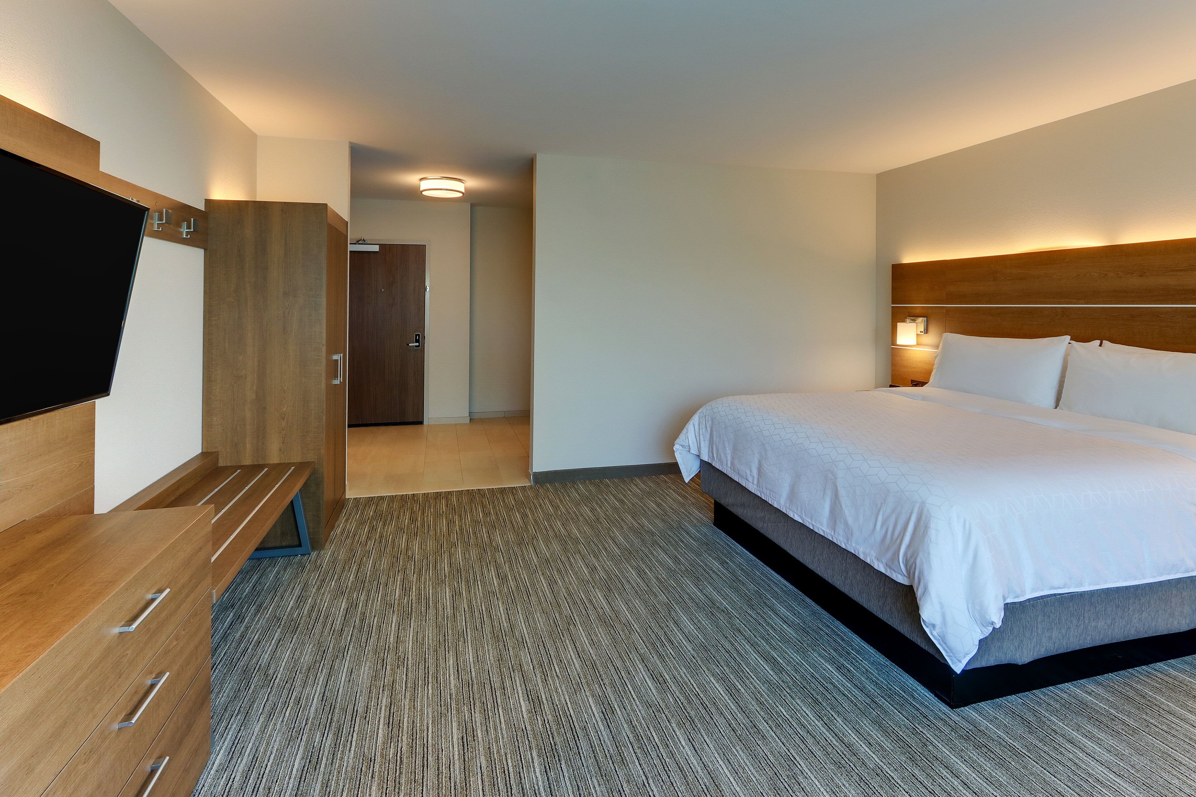 A hotel room with a bed, a TV, a wooden wardrobe, and a carpeted floor.