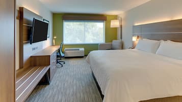 A hotel room with a bed, a desk with a chair, a flat-screen TV, a window, and a wall-mounted lamp.