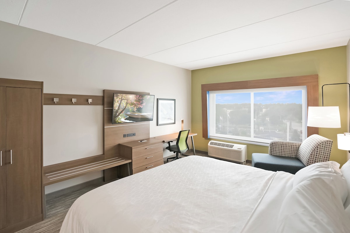 Habitación de hotel con cama, escritorio, silla, televisor y ventana con vista a la ciudad.