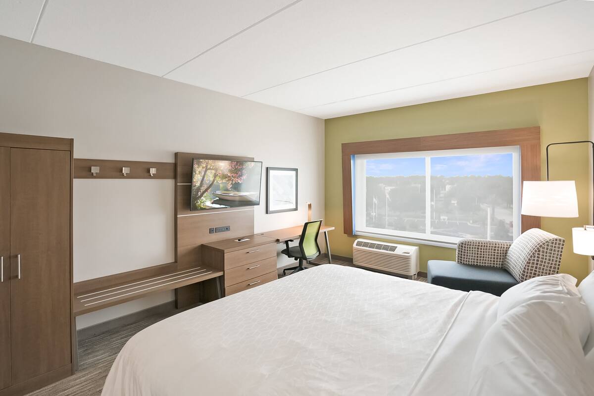 A hotel room with a bed, a desk, a chair, a TV, and a window with a view.