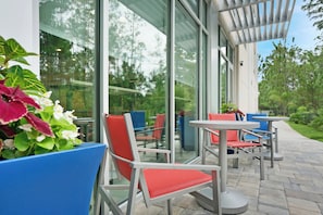 An outdoor seating area with glass walls, red and blue chairs, and potted plants.