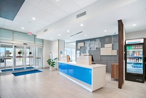 A reception area with a blue counter, a glass door entrance, a vending machine, and a potted plant. - Holiday Inn Express Jacksonville South Bartram Prk by IHG (Jacksonville)