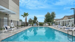 A rectangular swimming pool with a tiled deck, surrounded by a black metal fence. There are lounge chairs with blue cushions and white frames along the pool's edge. - Holiday Inn Express Jacksonville South Bartram Prk by IHG (Jacksonville)