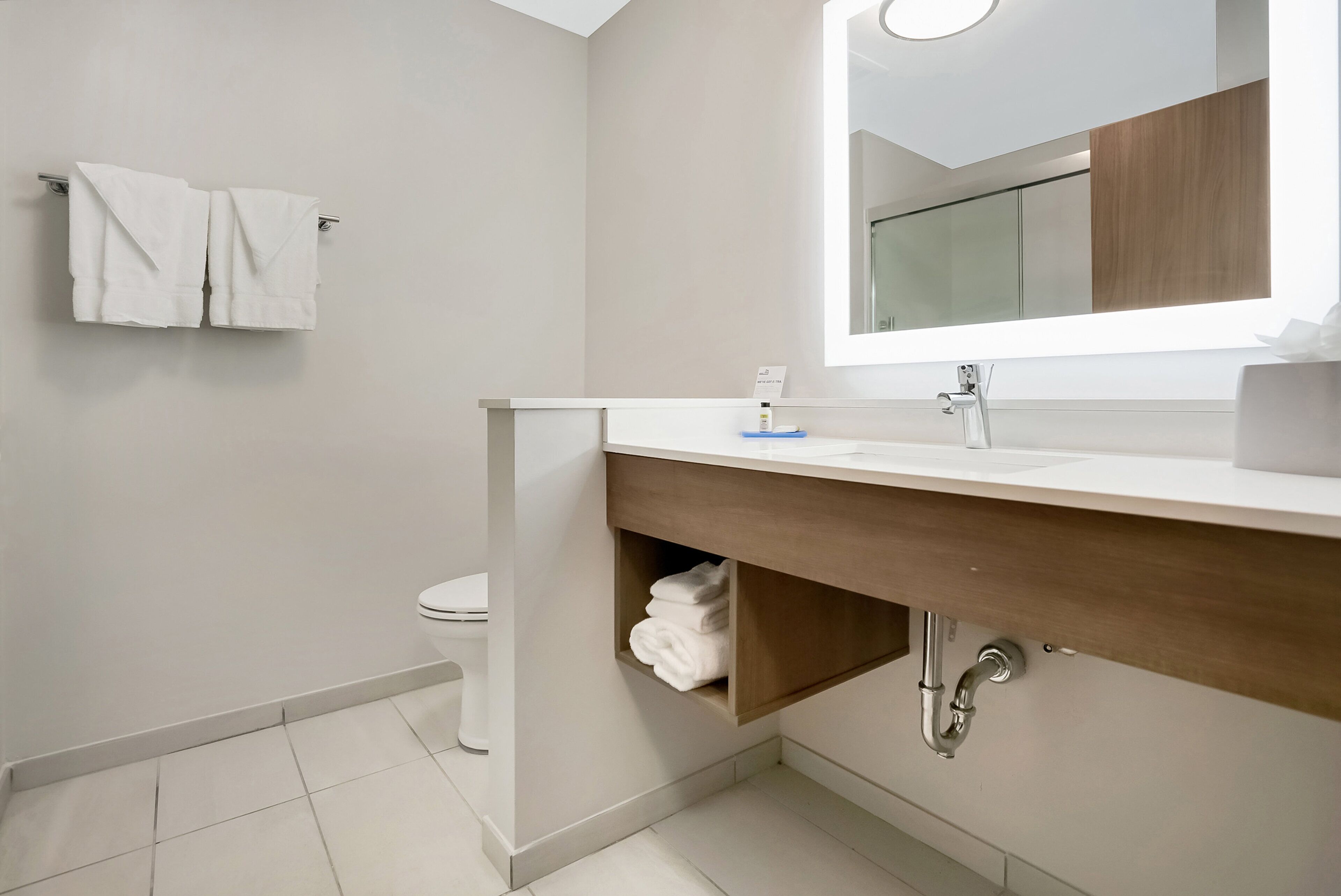 Un baño moderno con un lavamanos blanco, tocador de madera y un espejo encima.