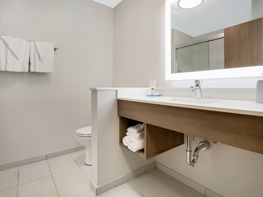 A modern bathroom with a white sink, wooden vanity, and a mirror above it.