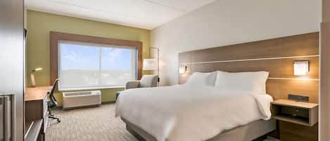 Quarto de hotel com uma cama grande, uma escrivaninha com cadeira, um abajur e uma janela com vista.