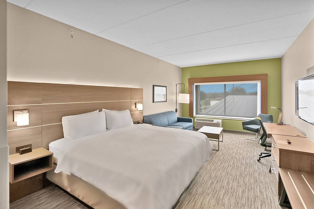 A hotel room with a large bed, a desk, a chair, a sofa, and a window with a view.