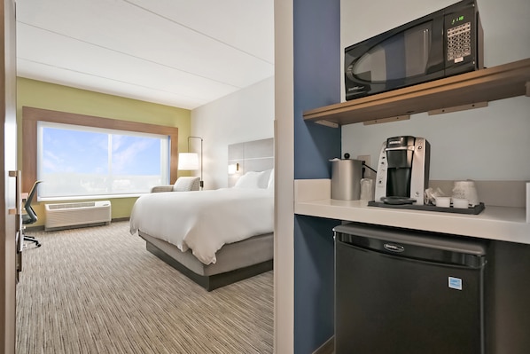 Habitación de hotel con una cama, un escritorio con microondas, cafetera y refrigerador pequeño.
