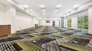 A spacious room with a patterned carpet, white walls, and a large window with a view of greenery.