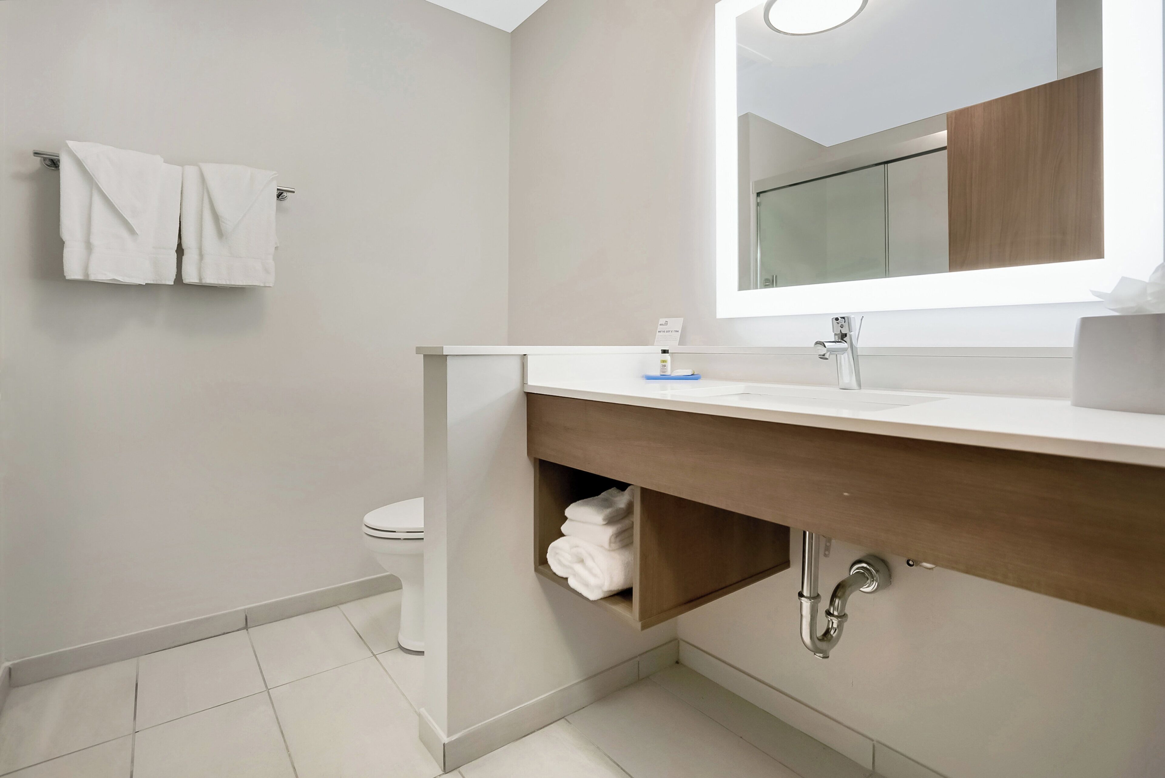 Un baño moderno con inodoro, lavamanos con espejo y perchero para toallas.