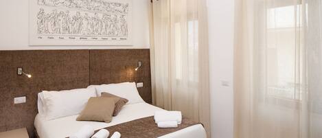 A neatly made bed with white and brown linens, a headboard with a framed artwork, and a bedside table with a lamp.