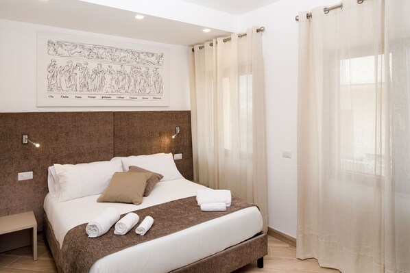 A neatly made bed with white and brown linens, a headboard with a framed artwork, and a bedside table with a lamp. - Le Muse Suite (Sorrento)