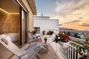 A balcony with a sun lounger, potted plants, and a view of the cityscape during sunset. - Le Muse Suite (Sorrento)