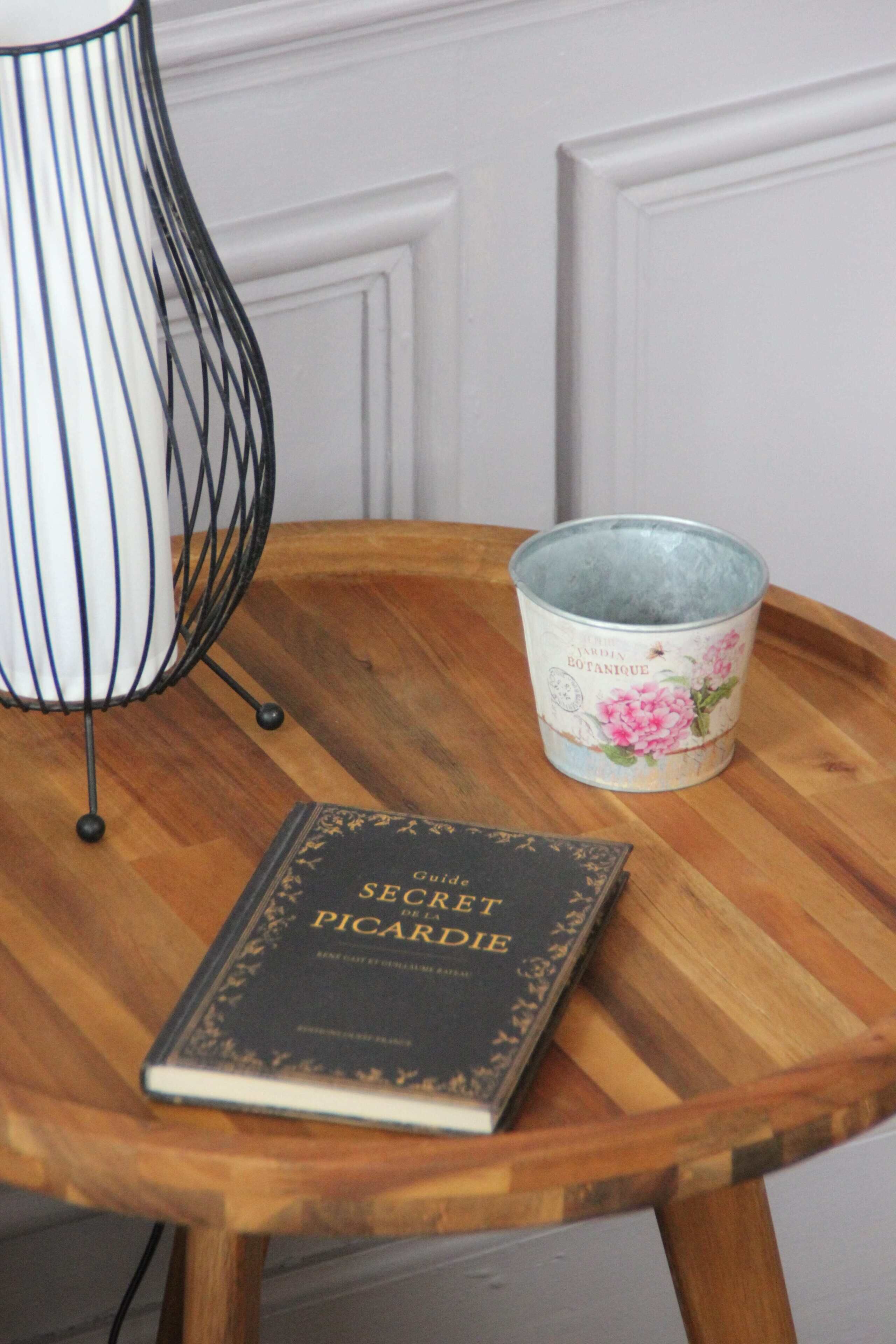 A book titled 'Guillaume Secret de la Picarodie' on a wooden table with a metal lamp and a tin canister with floral designs.