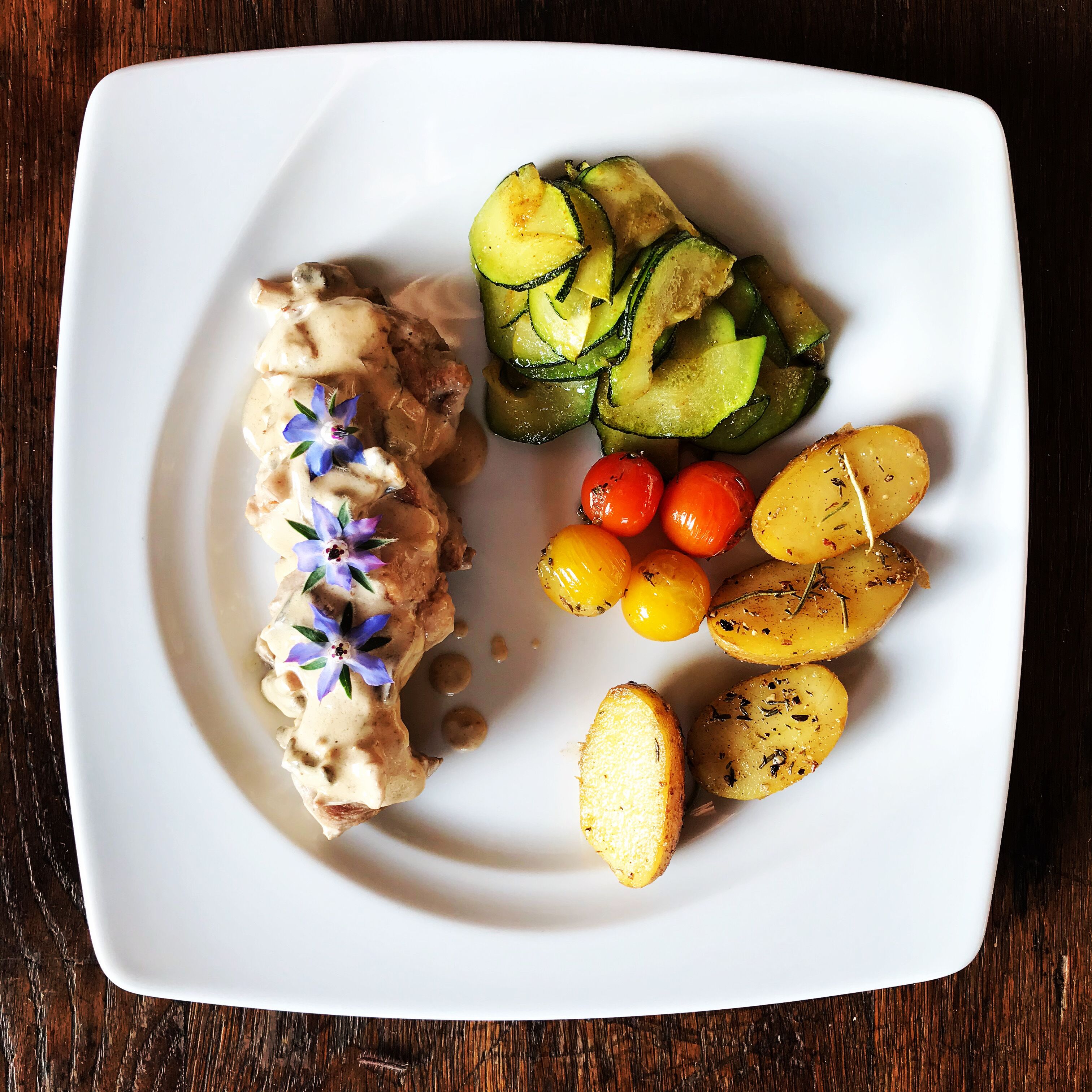 A white plate with grilled chicken, sliced zucchini, cherry tomatoes, and roasted potatoes.