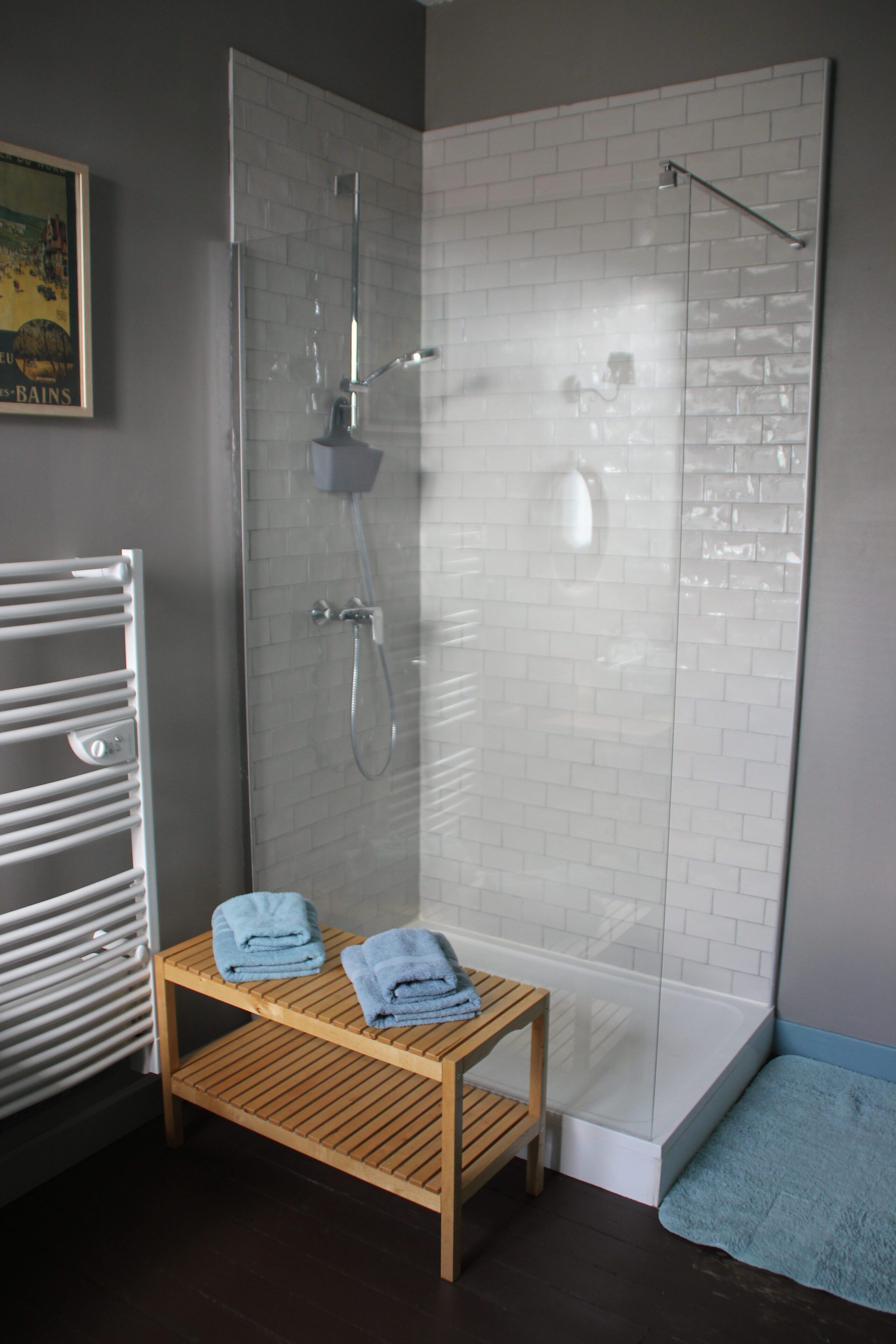 A shower area with a glass door, a wooden bench with towels, and a tiled wall.