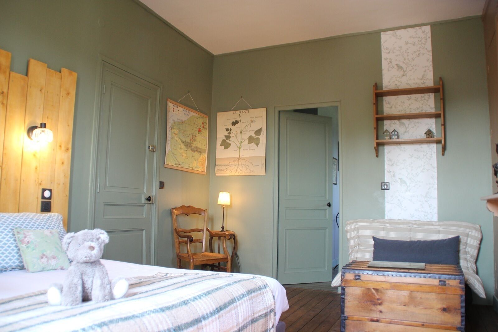 A bedroom with two beds, a wooden headboard, a map, a lamp, and a small shelf.