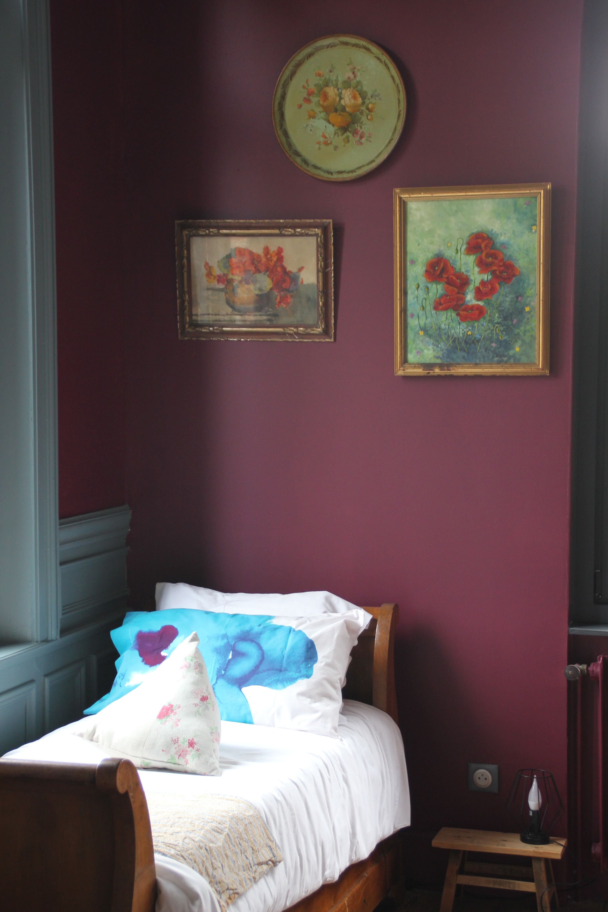 Une chambre à coucher comprenant un lit, une chaise, une petite table et deux œuvres d’art encadrées accrochées au mur.
