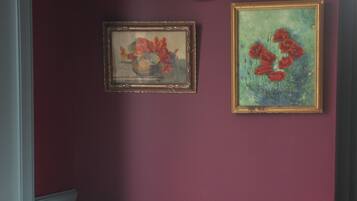 Une chambre à coucher comprenant un lit, une chaise, une petite table et deux œuvres d’art encadrées accrochées au mur.