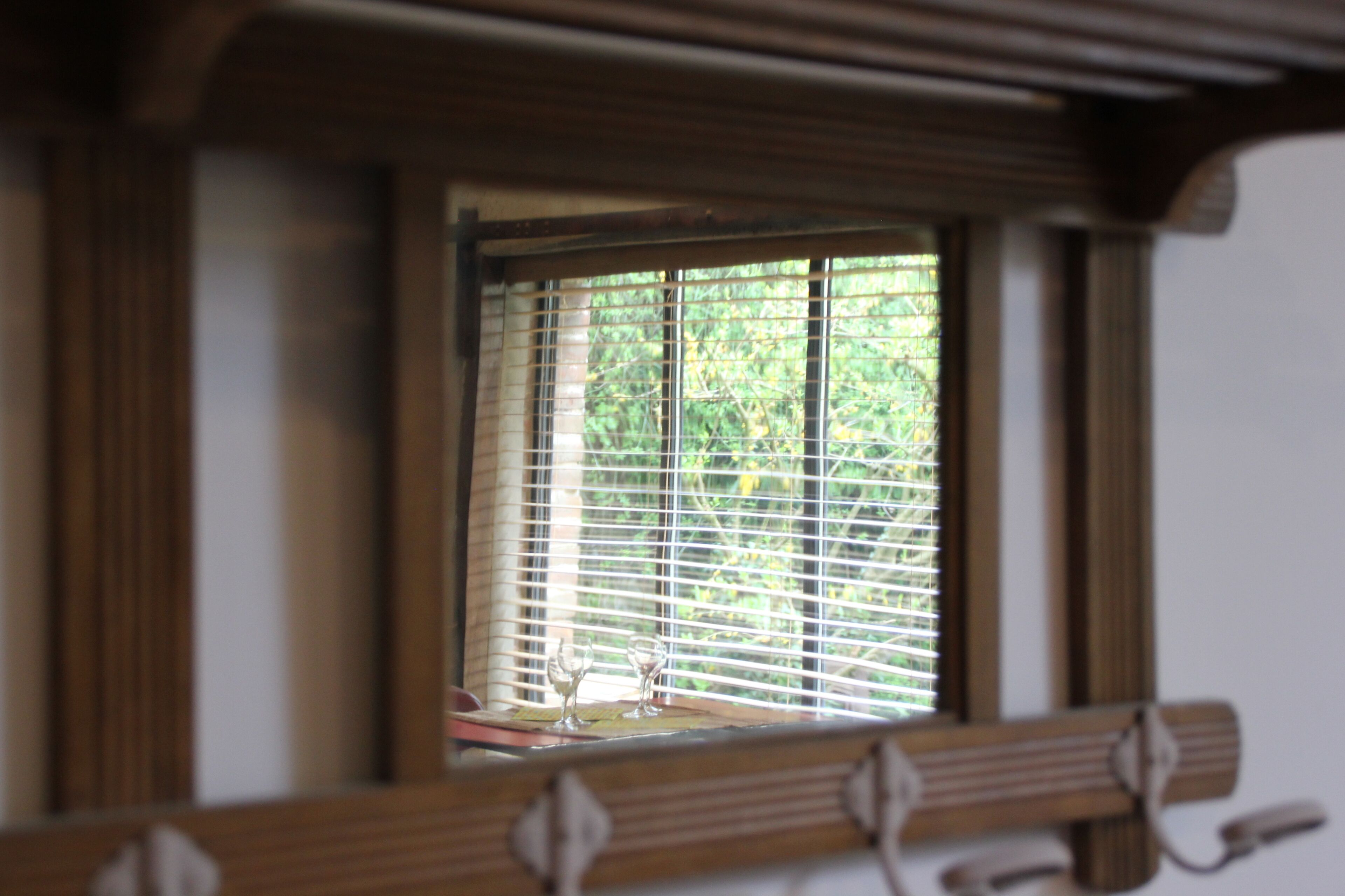 Una habitación con ventana que tiene persianas horizontales, un banco de madera y una pequeña mesa con dos copas de vino.