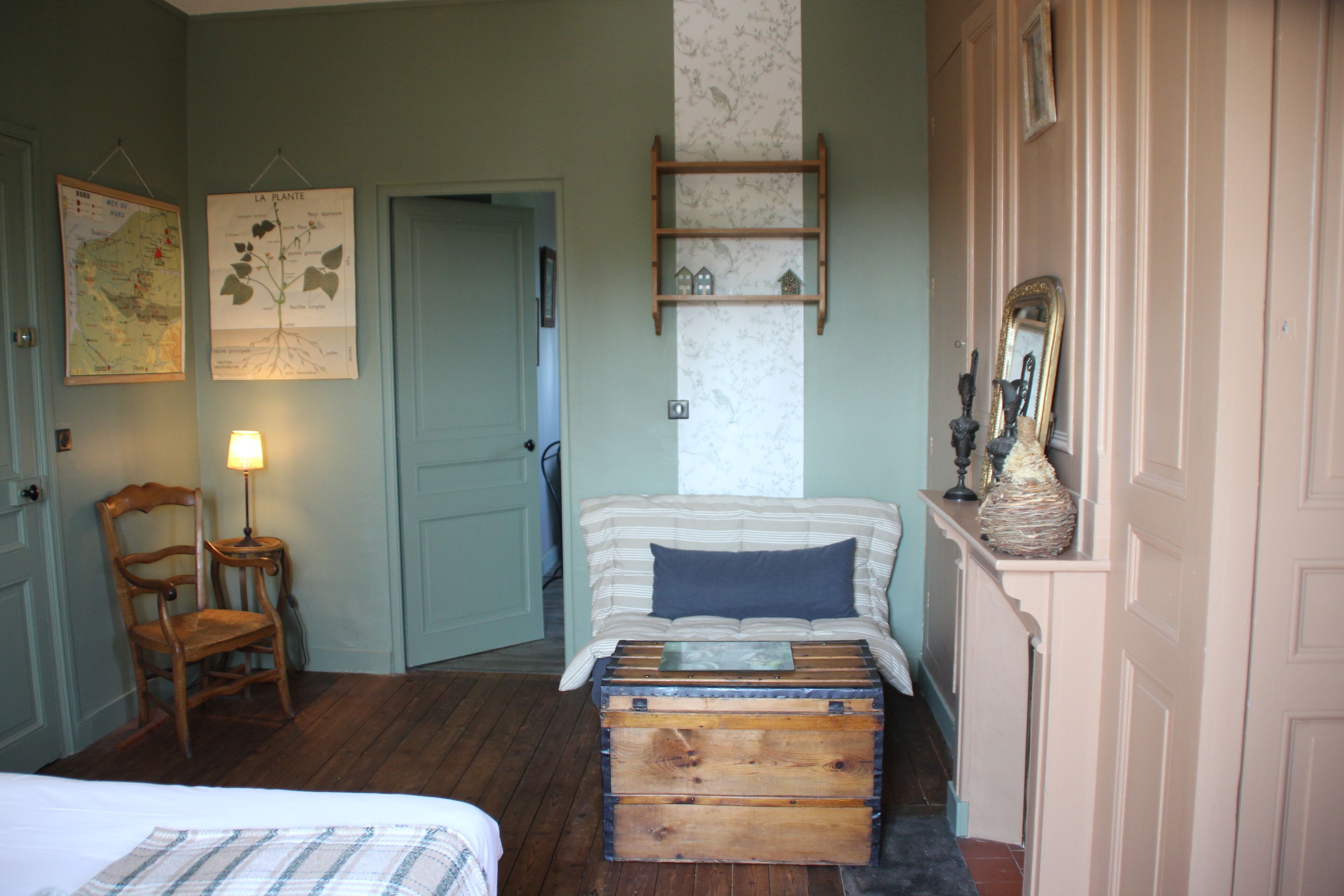 A room with a bed, a chair, a dresser, a map, and a mirror.