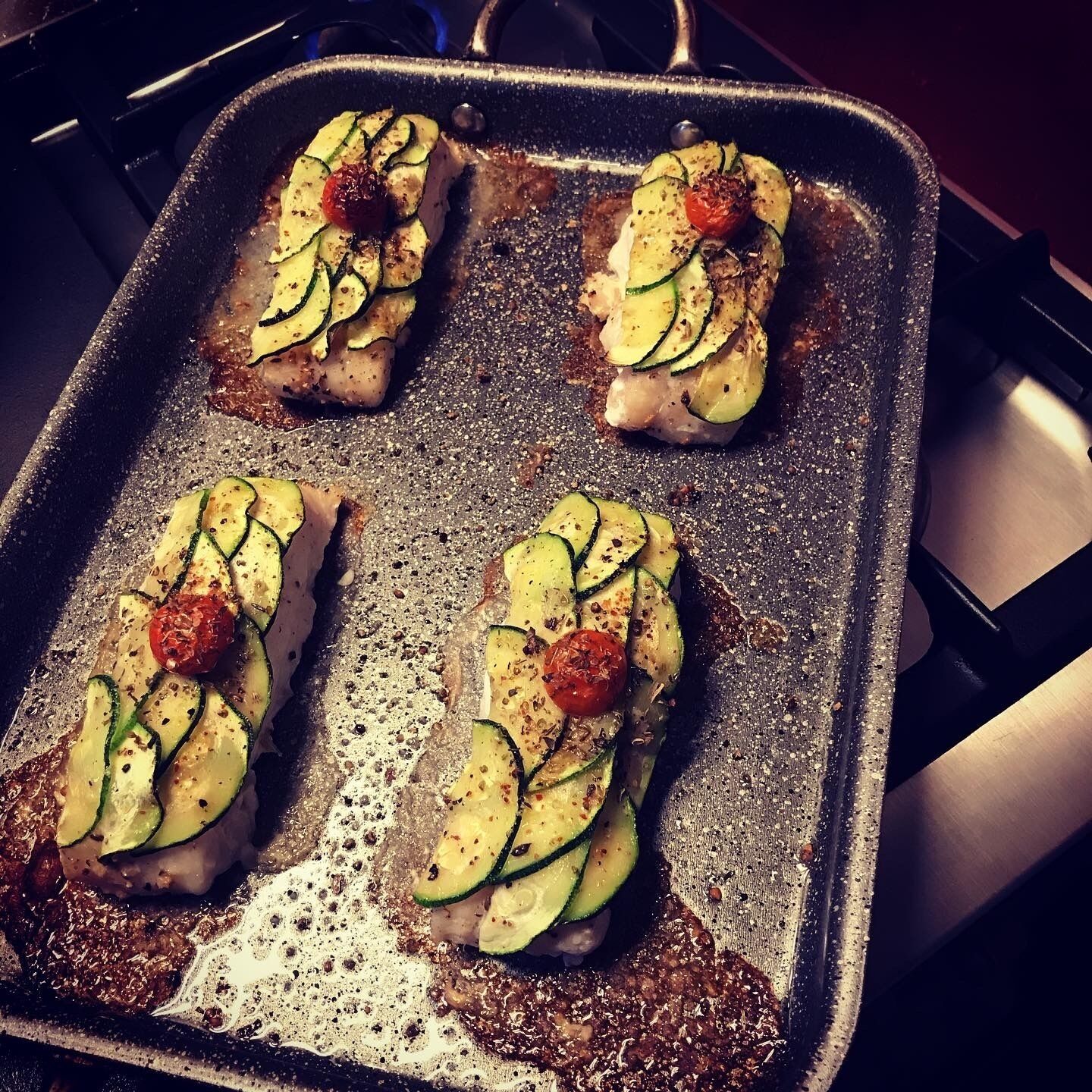 Een braadpan met vier stukken vlees, belegd met plakjes courgette en kerstomaatjes.