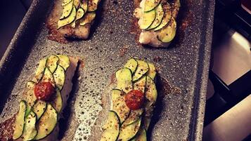 Een braadpan met vier stukken vlees, belegd met plakjes courgette en kerstomaatjes.