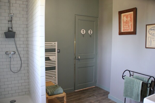 A bathroom with a shower, a door with two hooks, a towel rack, and a framed picture on the wall.