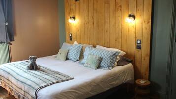 A bed with a striped blanket, multiple pillows, a teddy bear, and wooden headboard with wall-mounted lights.