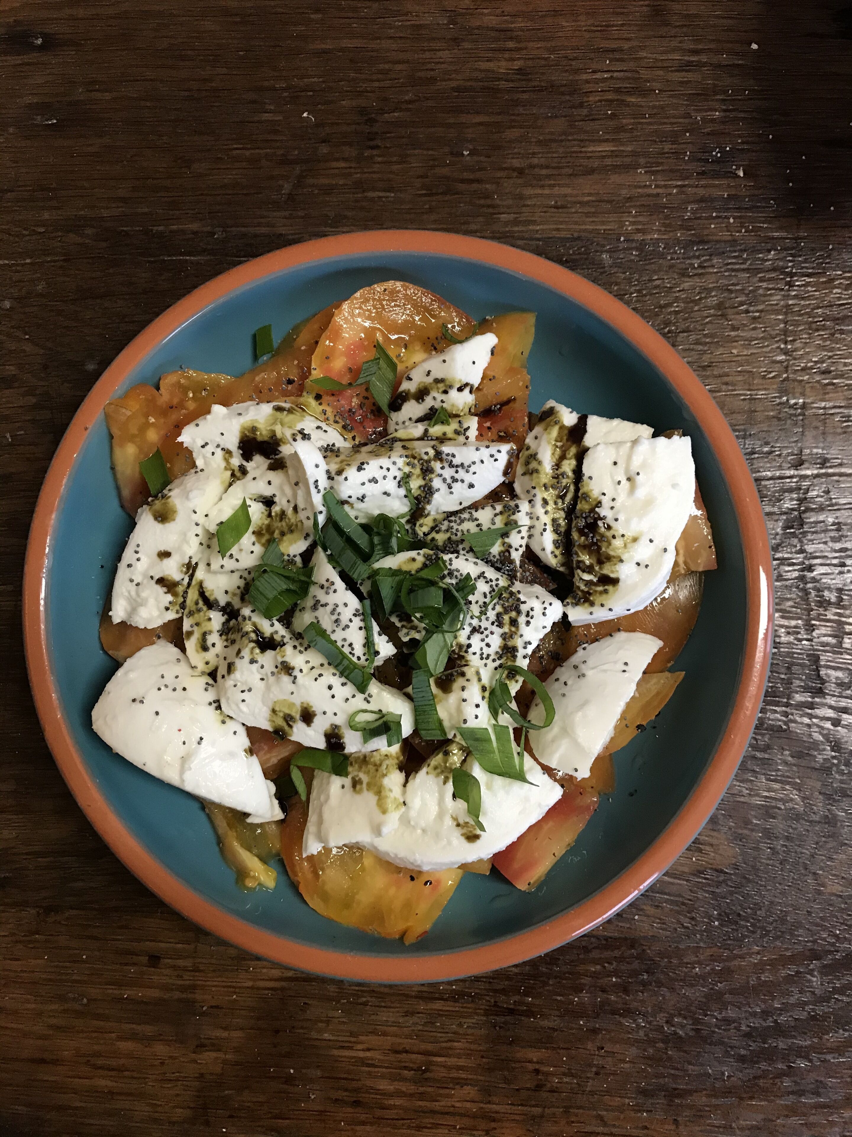 Un tazón de comida con mozzarella, tomates y cebollines sobre una mesa de madera.