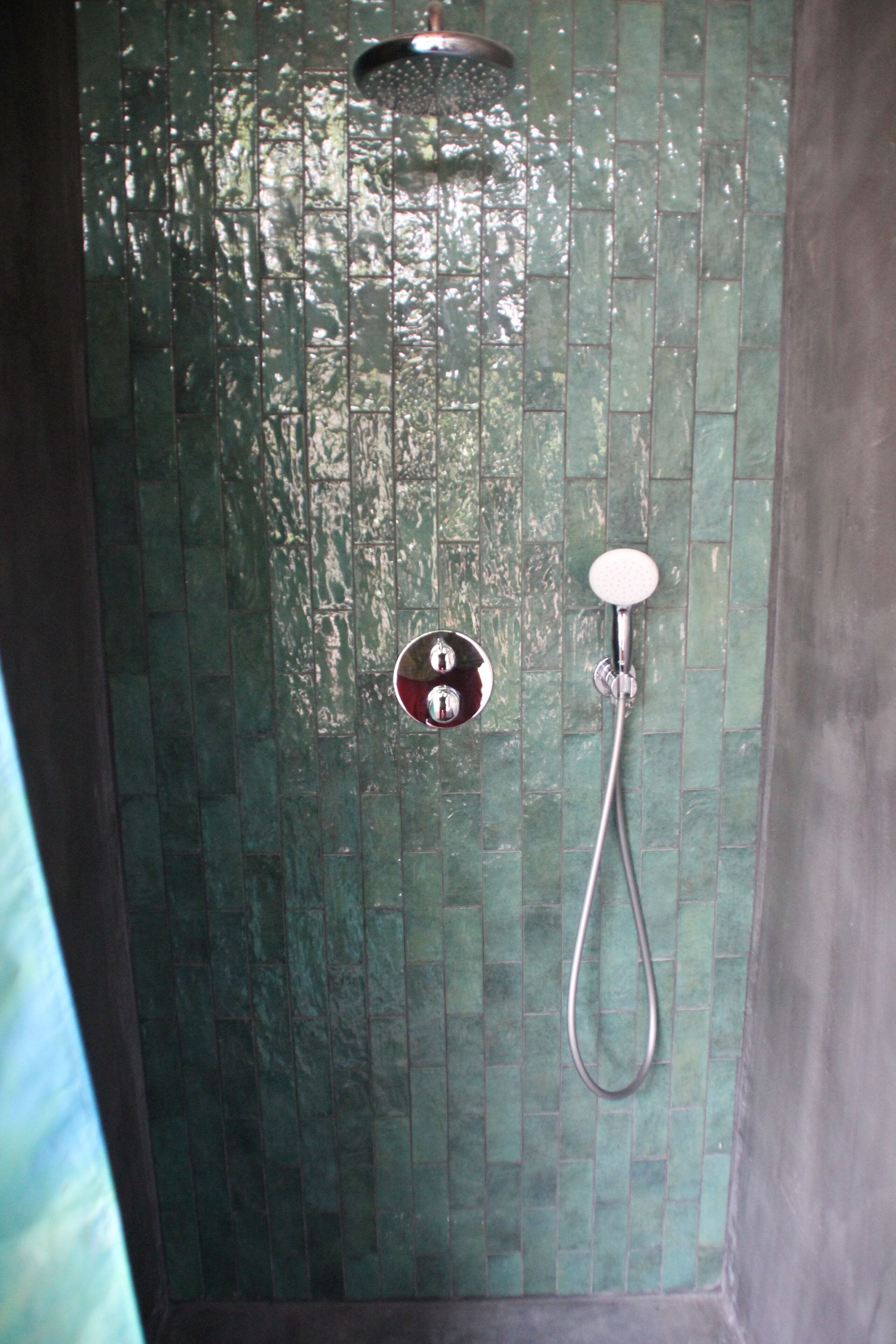 A shower with a handheld showerhead and a wall-mounted control.