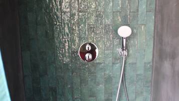 Een douche met een flexibele douchekop en een bediening aan de muur.