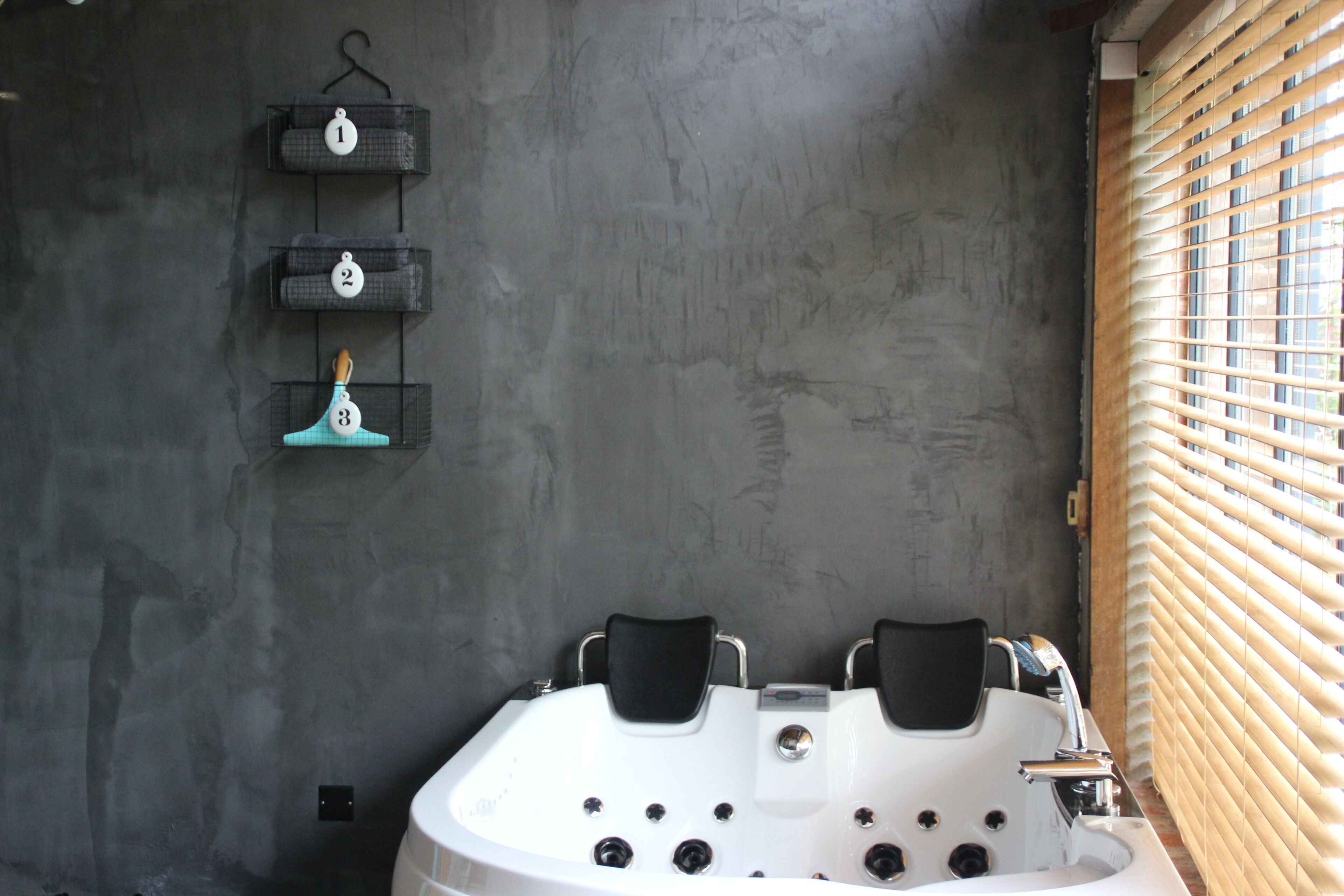 Un bagno moderno con una grande vasca, un portasciugamani con tre asciugamani e una finestra con persiane.