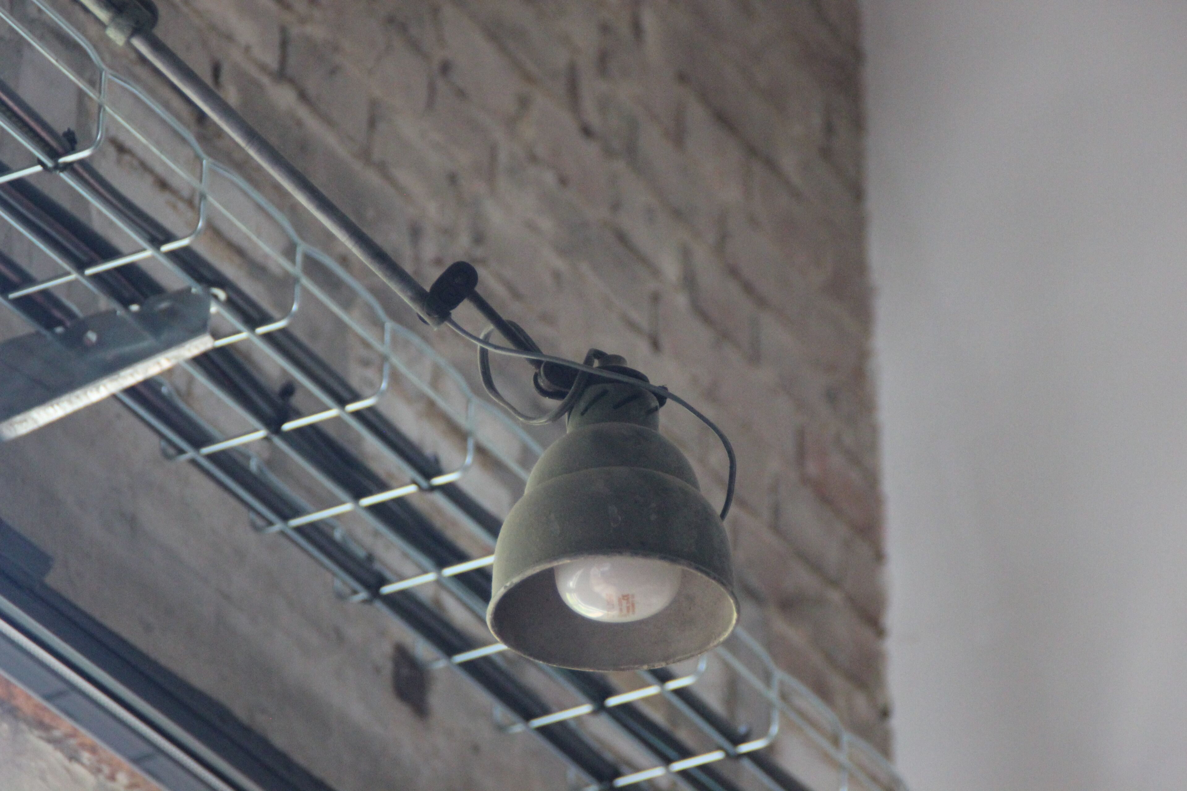 A hanging light fixture in a room with a brick wall and metal beams.