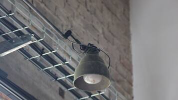 A hanging light fixture in a room with a brick wall and metal beams.