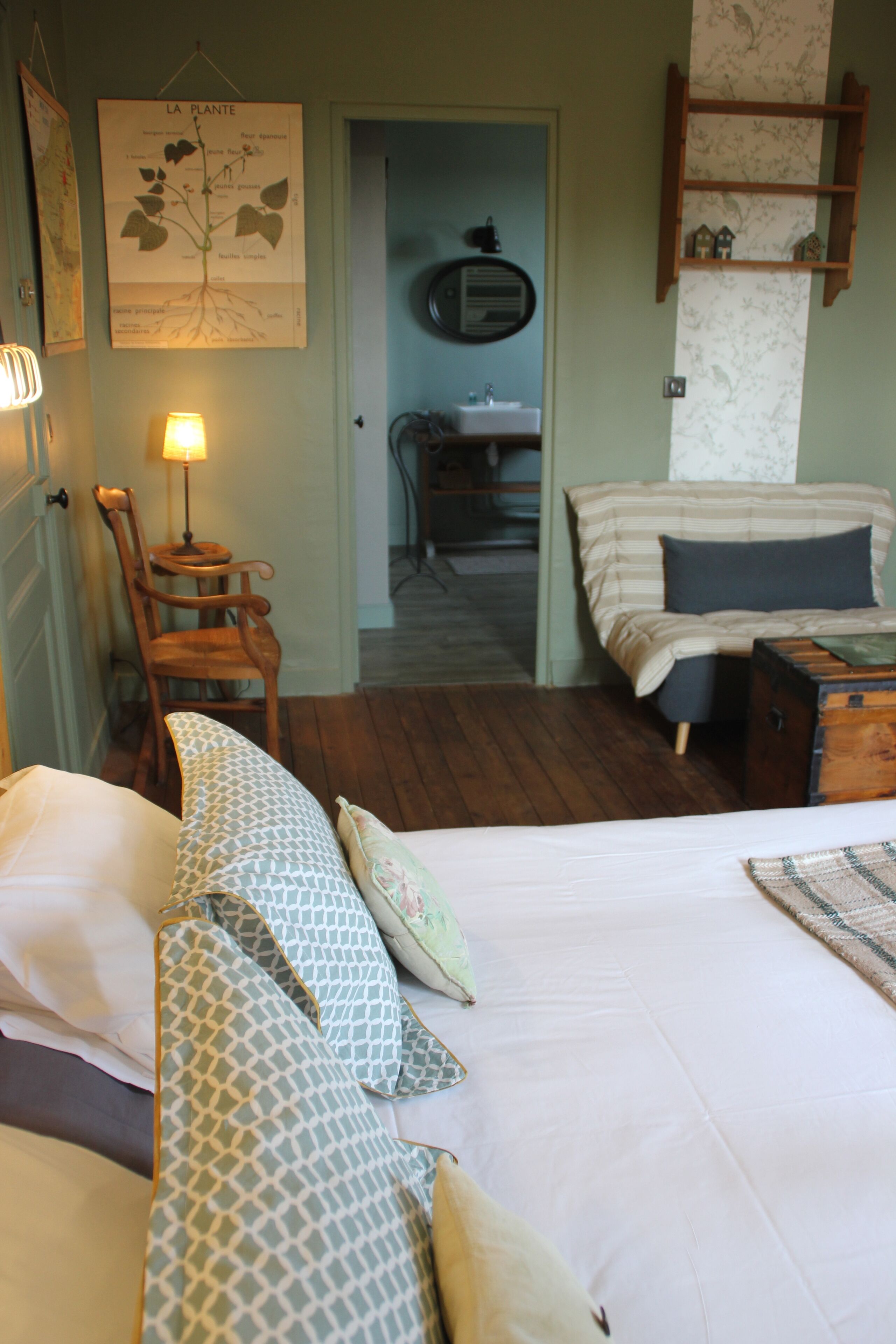 A bedroom with a bed, pillows, a wooden chair, a lamp, a dresser, and a wall-mounted shelf.