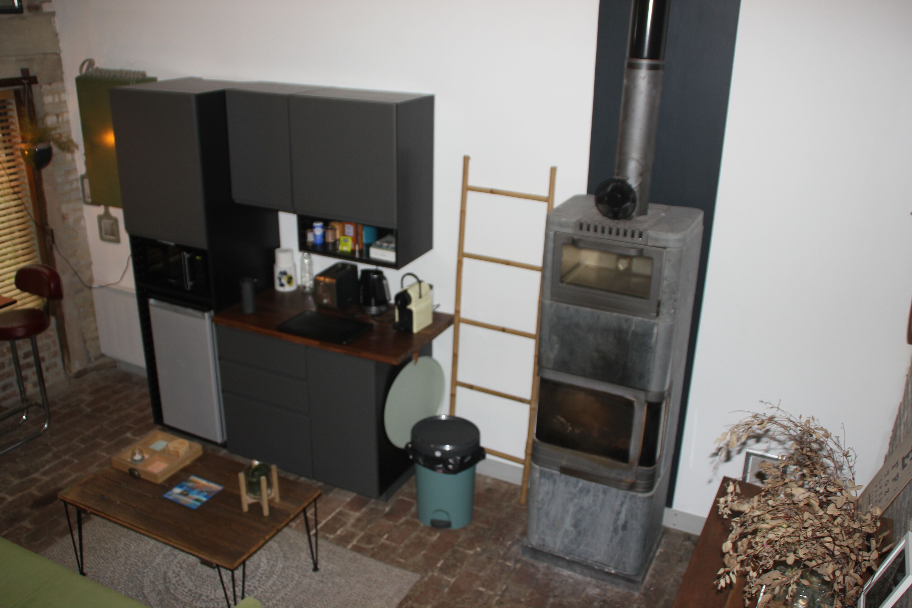 A compact kitchen with a built-in oven, a small trash bin, and a wooden table.