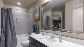 Une salle de bain moderne avec une baignoire, un grand miroir et un lavabo blanc.