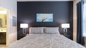 Une chambre à coucher avec un lit, deux tables de chevet avec des lampes, un tableau au mur et une fenêtre avec des rideaux.