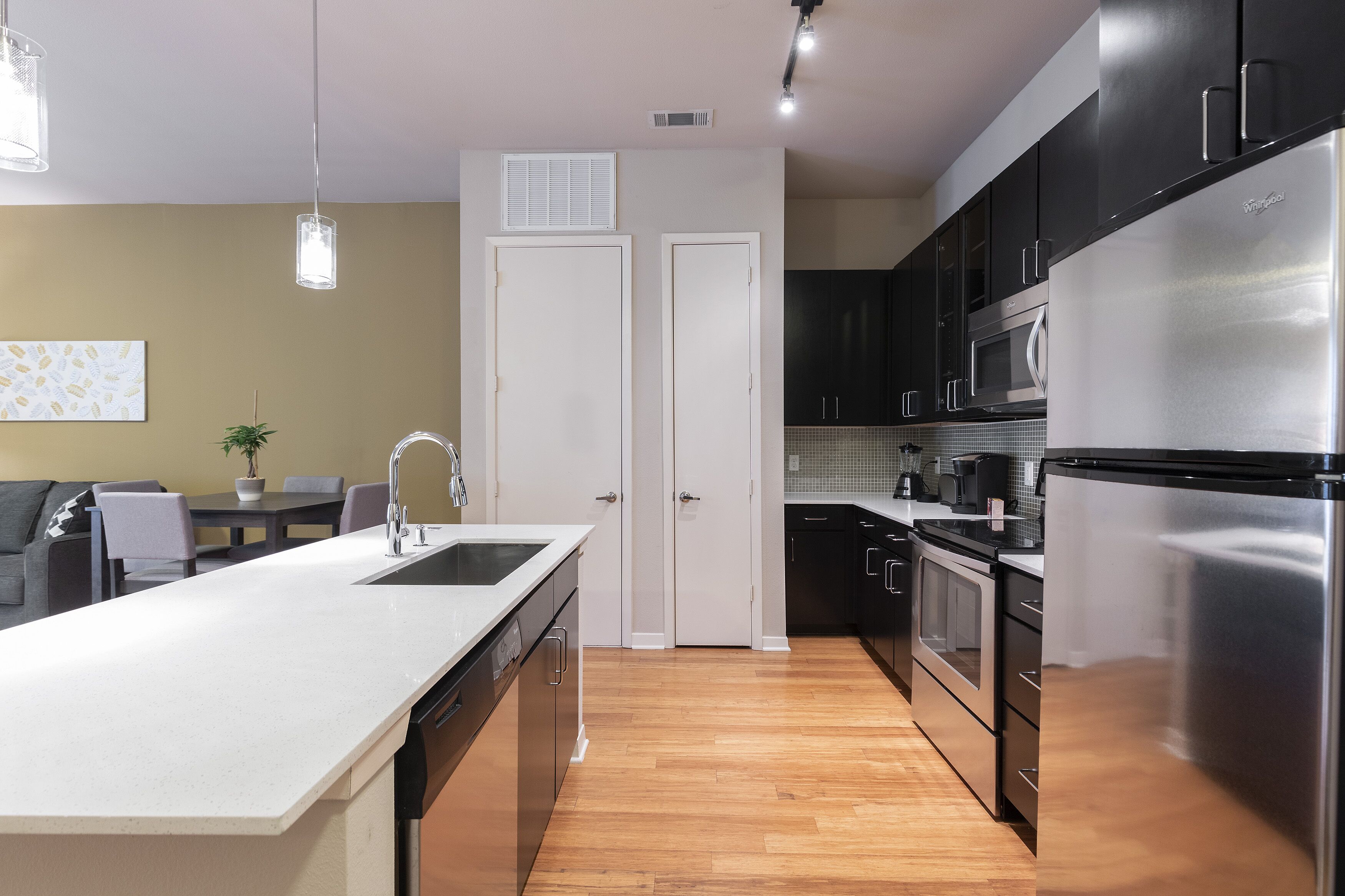 A modern kitchen with a central island, stainless steel appliances, and a dining area with a sofa and table.