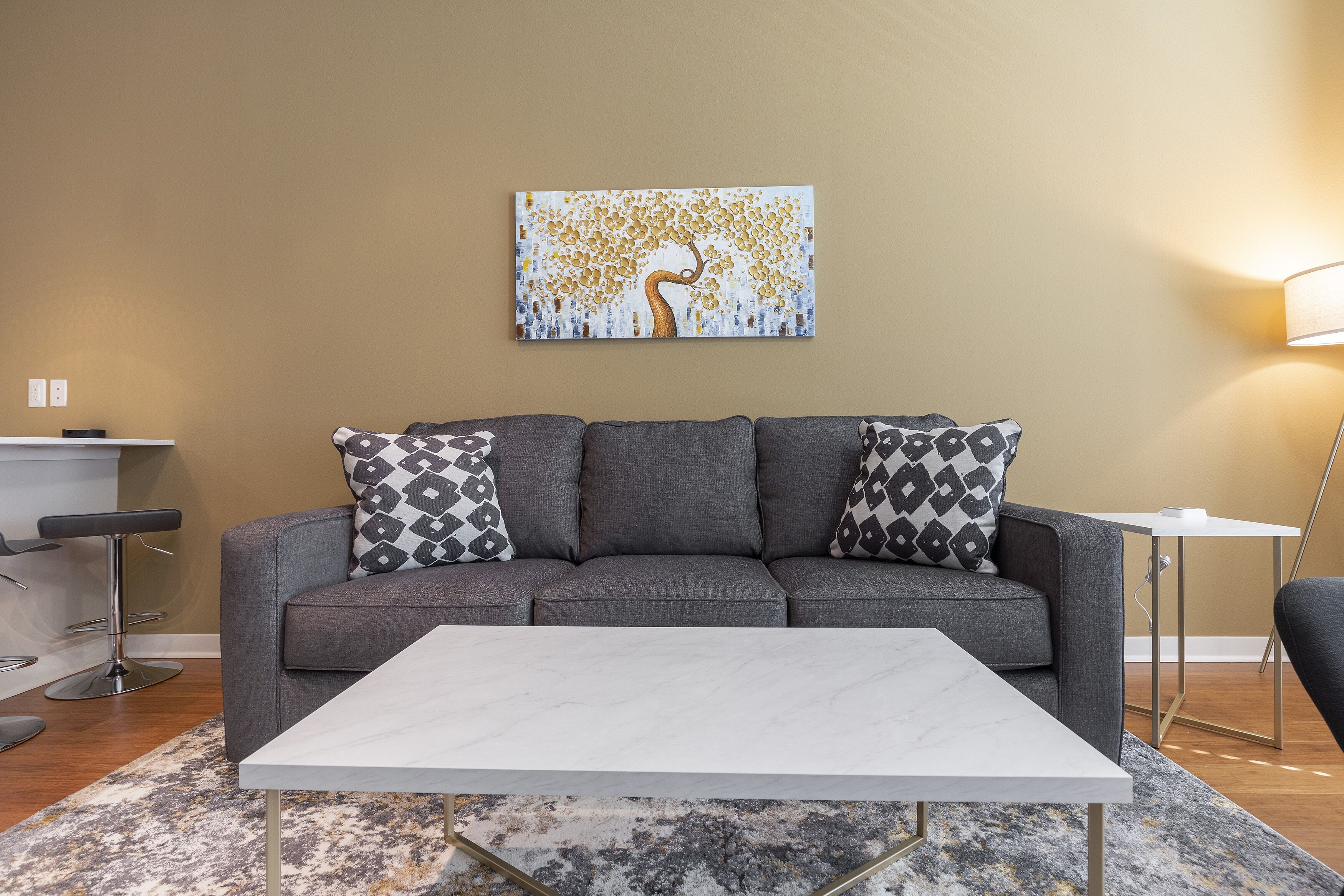 Una sala de estar moderna con un sofá gris, cojines estampados, una mesa de centro blanca y un cuadro en la pared.