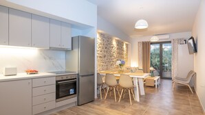 Eine moderne Küche mit weißen Schränken, einem Backofen und einem Kühlschrank. Es gibt einen Essbereich mit Tisch und Stühlen sowie eine Steinwand mit einem Fenster.