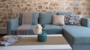 Ein Wohnzimmer mit einer Steinsäule, einem türkisfarbenen Sofa, gemusterten Kissen und einer Vase mit Blumen auf einem weißen Tisch.