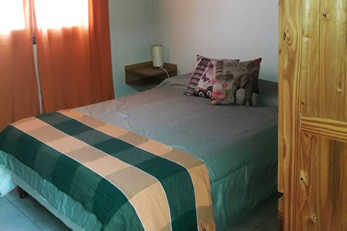 A bedroom with a bed, a wooden wardrobe, a nightstand, and a ceiling fan.